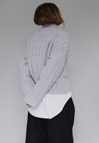 Szary sweter dziany o prążkowanej fakturze i wysokim kołnierzu, nałożony na białą koszulę, noszony z czarnymi spodniami. Widok z tyłu ukazuje luźny krój.