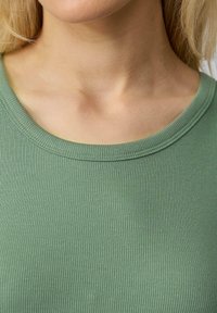 Groene geribbelde stoffen top met een brede halslijn, een gladde textuur en subtiele verticale lijnen, die tot aan het sleutelbeen reiken.