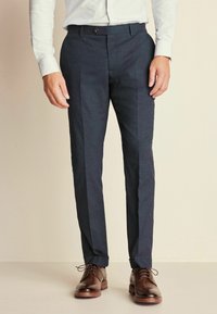 Pantalon ajusté bleu en tissu texturé, avec une coupe slim et une fine bande latérale, associé à des chaussures en cuir marron.