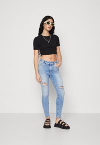 Black cropped t-shirt, light blue ripped skinny jeans, and black strappy sandals. Accessories include silver chain necklace and green sunglasses.