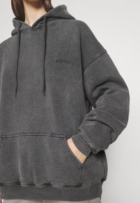 Hoodie grigio scuro realizzato in morbido misto cotone, con tasca frontale, cappuccio regolabile con cordino e discreta branding ricamata sul petto.
