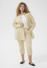 Žlutá a bílá pruhovaná košile s knoflíky doplněná odpovídajícími zkrácenými kalhotami. Hladký materiál a volný střih. Černé baleríny.