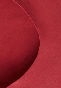 Revêtement en tissu rouge incurvé avec une texture lisse et un détail de couture subtil le long du bord.
