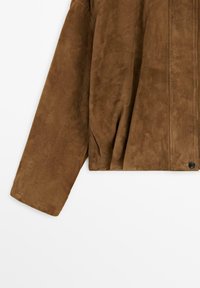 Giacca di pelle scamosciata marrone con maniche lunghe e cuciture visibili, caratterizzata da una chiusura con bottoni nella parte anteriore inferiore.