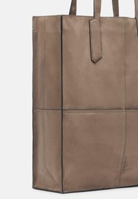 Tote bag in zachte taupe leren met een matte afwerking. Beschikt over een gestructureerde vorm, handvatten aan de bovenkant, subtiele stiksels en een merkdetail aan de onderkant.