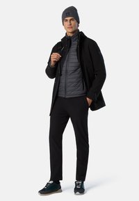Giacca esterna nera, gilet imbottito grigio, pantaloni neri e sneakers scure. Berretto lavorato a maglia grigio, ferramenta funzionale, design elegante.