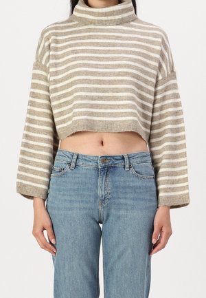 Femme portant un pull court à col roulé rayé beige et blanc et un jean taille haute bleu clair, debout avec les bras détendus.