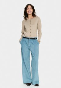 Beidža pogāžas kardigāns ar ribota tekstūra, apvienots ar gaiši ziliem platām apakšbiksēm un melnu jostu.