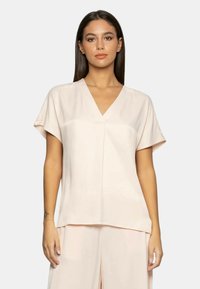 Blusa corta a maniche corte color rosa chiaro con scollatura a V, realizzata in tessuto morbido, con vestibilità ampia e discreti dettagli plissettati sul davanti.