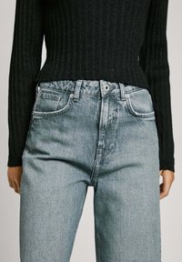 Ljusblå högmidjade jeans med rak passform, utrustade med klassisk femfickdesign och metallknappsstängning, kombinerat med en svart ribbad tröja.