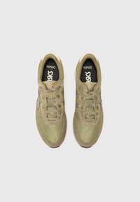 Olive green sneakers with a mesh and suede upper, featuring laces, a padded tongue, and a black "Asics" logo on the insole.