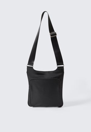 Black crossbody bag with adjustable shoulder strap and front zippered pocket against plain light background.