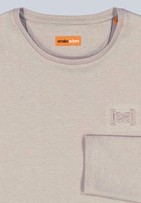 Hellgraues Langarmshirt mit rundem Halsausschnitt. Verfügt über ein gesticktes Logo auf der Brust und einen glatten, strukturierten Stoff.