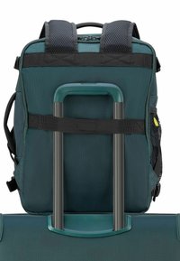 Zaino in tessuto verde con spallacci imbottiti, dotato di una maniglia retrattile argentata integrata in una valigia sottostante.