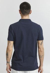 Námořnická modrá polo tričko vyrobené z bavlny, s klasickým límcem, krátkými rukávy a přiléhavým střihem. Jednoduchý design bez vzorů.