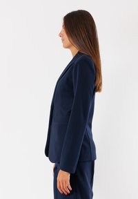 Blazer tailored blu navy con un design strutturato, chiusura con un bottone e due tasche frontali, realizzato in tessuto liscio.