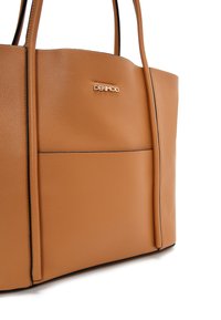 Tan leren totebag met een gestructureerde vorm, voorzien van een voorvak, zwarte afwerking en een gouden logoaccent aan de zijkant.