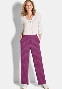 Fuchsia weit geschnittene Hosen mit einem Diamantmuster, kombiniert mit einer weißen Langarmbluse. Die Hose verfügt über Taschen und einen komfortablen Bund.