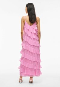 Rosa chiffong maxi-klänning med lager av volanger, v-formad ryggdesign och tunna spagettiband. Har en flödande siluett och genomskinlig textur.