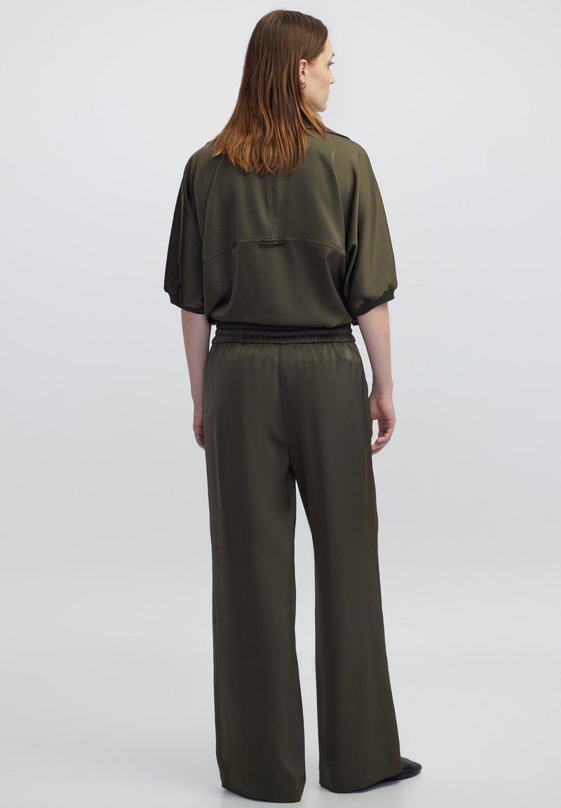 Olijfgroen outfit met een losse top met korte mouwen en wijde broekspijpen, beide in glad, glanzend stof met een elastische tailleband.