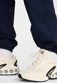 Hvide sneakers med mesh-overdel, sorte accenter og klar luftpolstring. Vist sammen med marineblå joggers og hvide sokker.