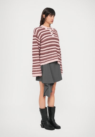 Ριγέ πουλόβερ σε ροζ και βουργουνδί αποχρώσεις με γιακά και κουμπιά, συνδυασμένο με γκρι ασύμμετρη φούστα και μαύρα μποτάκια αστραγάλου.