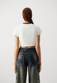 Witte cropped t-shirt met zwarte accent kraag, gecombineerd met hoge, donkerblauwe, vervaagde cargo jeans met grote achterzakken.