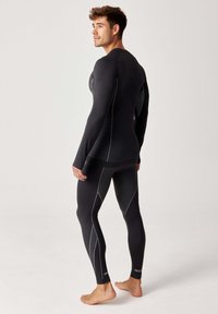 Czarna sportowa warstwa bazowa z długim rękawem i legginsami, z kontrastującymi białymi szwami, dopasowanym krojem oraz teksturowaną tylną częścią.