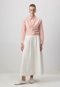 Light pink long-sleeve wrap shirt with collar, paired with a flowing white maxi skirt and white lace-up shoes. Simple design, smooth texture.