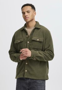 Grüne Fleece-Hemdjacke mit zwei Brusttaschen, Knopfverschlüssen und lockerer Passform. Mit einem kragen und weichem Material.
