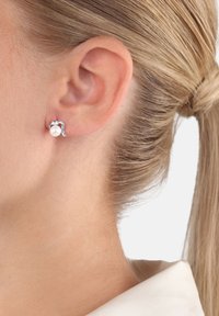 Silverörhänge med en böljande design och en vit pärla som accent. Fästet har en slät, polerad yta.