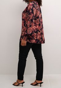 Blusa de manga larga en marino con un patrón floral en rosa, combinada con jeans ajustados negros y tacones de dedo al aire negros, mostrada de lado.