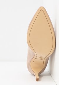 Light pink suede high heel shoe with a pointed toe and slender stiletto heel, featuring a smooth sole and minimalistic design.