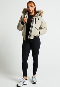 Bežs pūkains džemperis ar kažokādas oderi kapuci, priekšējā rāvējslēdzēja aizdarīšana un divas sānu kabatas. Savienots ar melnajām legingām un sporta apaviem.