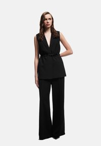 Zwarte zondermouw blazer met een diepe V-hals en bijpassende wijde broek, afgewerkt met een tailleband, van gladde stof en met een minimalistisch ontwerp.