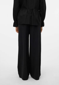 Czarna lekka bluzka ze ściąganym w talii pasem i długimi rękawami, zestawiona z szerokimi czarnymi spodniami. Gładka tekstura z subtelnym ruchem.