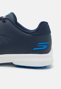 Marineblaue Golfschuhe aus synthetischem Material; ausgestattet mit einem strukturierten Mesh-Kragen, weißer Sohle und blauem Akzent-Logo an der Seite.