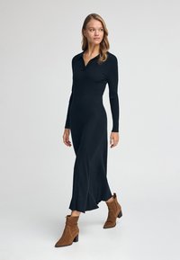 Svart ribbad klänning med krage, långa ärmar och utsvängd nederdel. Kombinerad med bruna mocka ankelstövlar med klack.