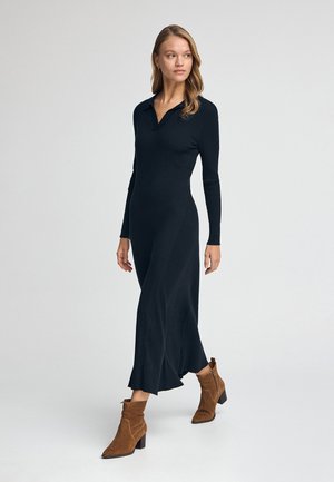 Robe noire à rainures avec un col, des manches longues et un ourlet évasé. Assortie à des bottines en cuir suédé marron avec un talon bloc.