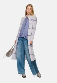 Light gray long cardigan with stripes, ruffled lavender blouse, wide blue jeans, and gray handbag. Flat black shoes complete the outfit.