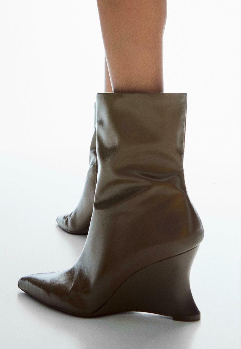 Botine cu toc wedge în verde măsliniu închis, fabricate din material sintetic lucios, având vârf ascuțit și un design lasat al brâului.
