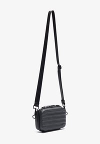 Sort crossbody taske med en tekstureret, ribbet overflade, lynlåslukning og justerbar rem. Kompakt design, der passer til det nødvendige.