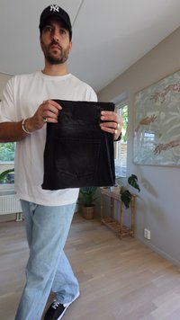 Jeans de mezclilla negros en alto, con un bolsillo trasero y una banda de cintura texturizada. La tela muestra un ligero desgaste, indicando un uso regular.