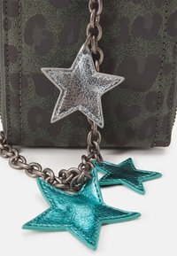 Łańcuszek z metalicznie srebrnymi i turkusowymi charmsami w kształcie gwiazdek przymocowanymi do zielonego tła z fakturą leoparda.