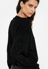 Musthave mustriba, millel on struktuursed detailid, soonilised aktsendid ja lõdvestatud lõige. Materjal näib pehme ja sellel on tagasihoidlik läige.