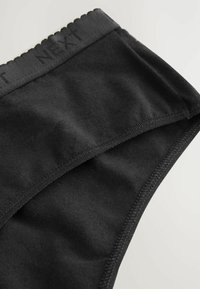Culotte en coton noire avec une taille à volants. Présente une texture lisse et des coutures surpiquées pour la durabilité. Le logo est subtilement embossé sur la taille.