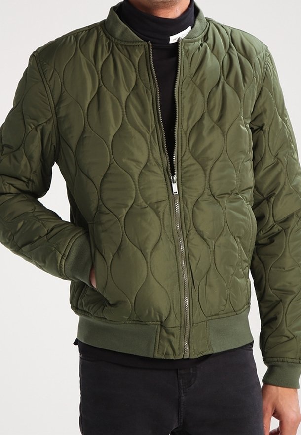 Oliwkowa pikowana kurtka typu bomber z prążkowanym kołnierzem i mankietami, wyposażona w centralny zamek błyskawiczny oraz boczne kieszenie. Miękki, teksturowany materiał.