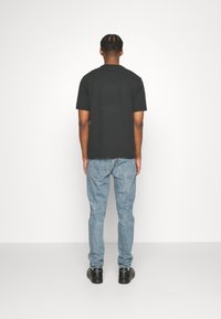 Camiseta de algodón negra con mangas cortas, combinada con jeans de mezclilla azul claro. Los zapatos son negros con un logo. Conjunto sencillo y casual visto desde atrás.