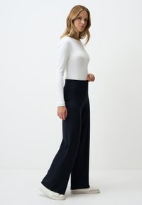 Pantalons noirs à_large taille en tissu doux, avec une ceinture haute et une texture lisse, associés à un haut ajusté à manches longues blanc.