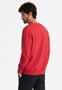 Sudadera roja de manga larga, con puños y dobladillo acanalados, cuello redondo, hecha de un material texturizado, mostrada desde la parte de atrás.